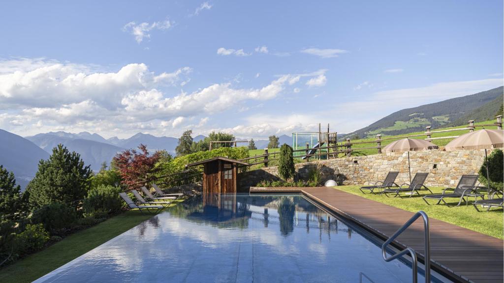 aussenpool-mit-sonnenliegen-bergpanorama-und-gruenem-garten-an-einem-sonnigen-tag.jpg